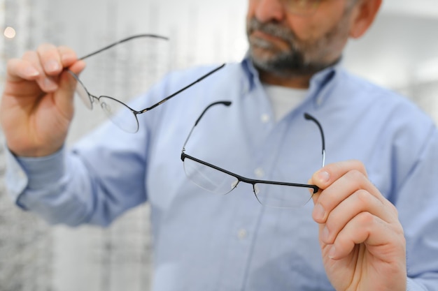 Un homme âgé choisissant des lunettes dans un magasin d'optique essaie des montures de lunettes pour décider de la parfaite