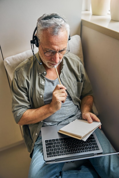 Homme âgé concentré dans des lunettes et des écouteurs travaillant à domicile