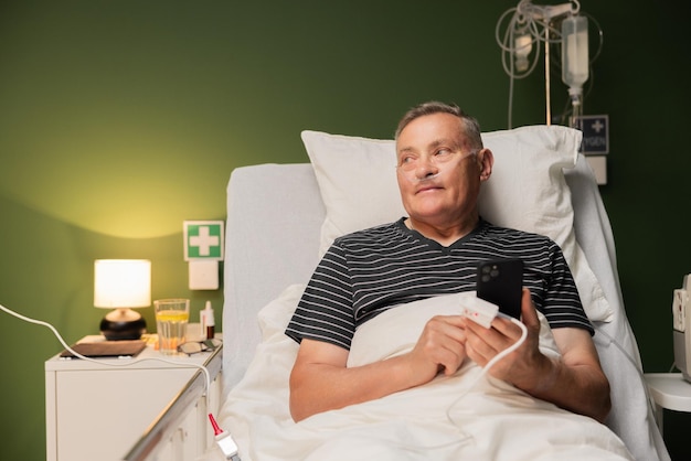 Un homme âgé dans un lit d'hôpital utilisant un tube d'oxygène et surveillant ses niveaux d'oxydation avec un dispositif de mesure de l'oxygènes au doigt