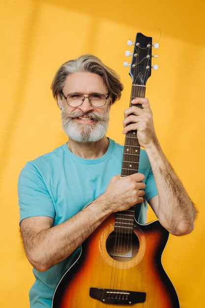 Homme âgé dans des lunettes et des écouteurs jouant de la guitare sur fond jaune Prise de vue en studio