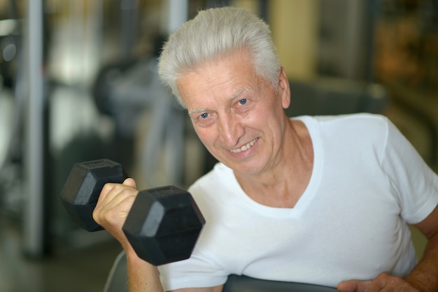 Homme âgé dans une salle de sport. faire de l'exercice avec des haltères