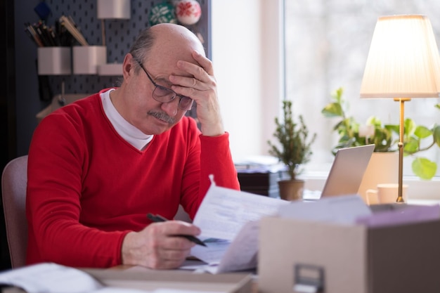 Un homme âgé déprimé s'inquiète du problème financier. Un homme âgé désespéré et stressé qui a l'air frustré par la paperasserie et les factures pense à la dette d'argent