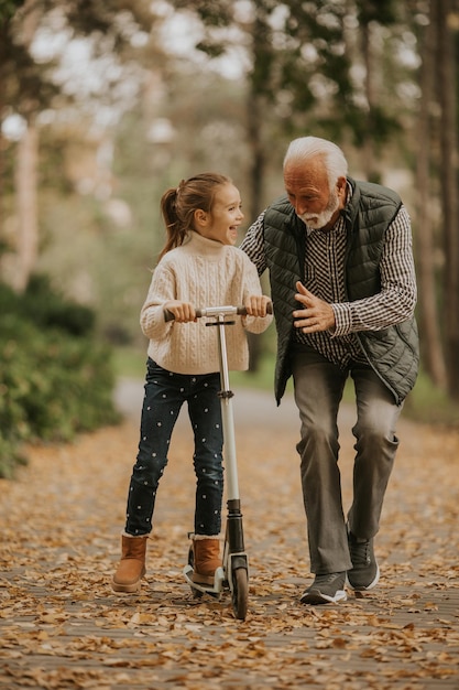 Photo homme âgé enseignant à sa petite-fille comment faire du scooter dans le parc