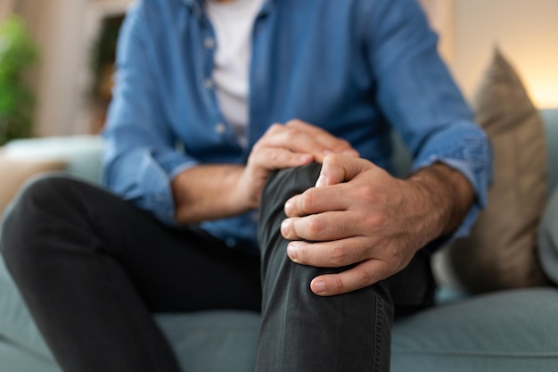 Photo l'homme âgé est assis sur le canapé à la maison a une douleur dans l'articulation du genou tenant sa jambe concept d'arthrose