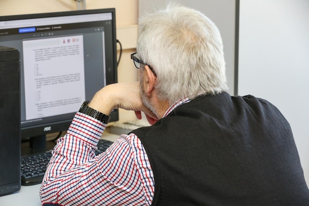 un homme âgé est assis devant un ordinateur vue de dos