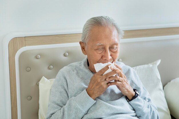 Homme âgé éternuant sur le lit