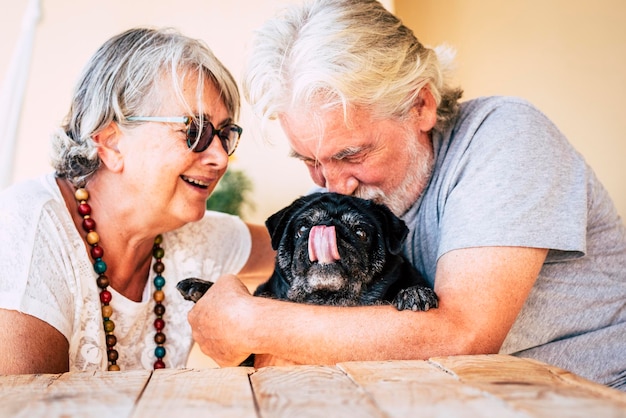 Un homme âgé avec une femme embrassant un chien alors qu'il est assis à la maison