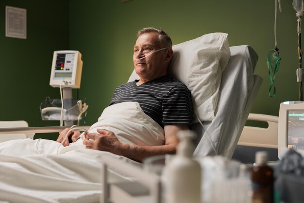 Homme âgé hospitalisé avec un tube d'oxygène et un moniteur d'oxydation au bout du doigt après une opération