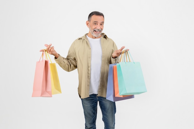 Un homme âgé joyeux tenant des sacs d'achat colorés dans deux mains