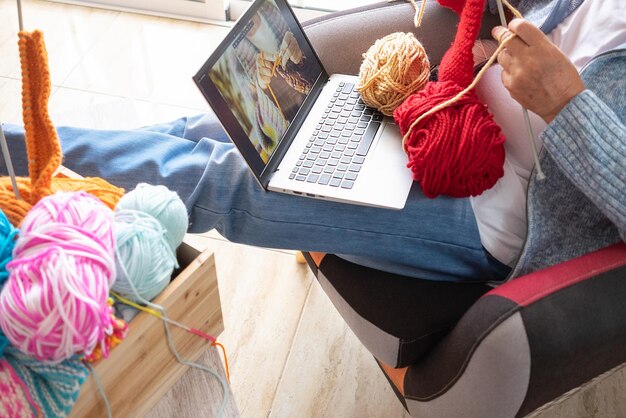 Photo un homme âgé à la maison suit un didacticiel de tricot en ligne pour apprendre à tricoter et profiter d'une activité de loisirs assis sur le fauteuil des hommes tricotant avec l'aide d'un cours d'informatique