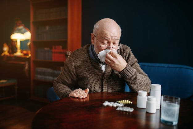 Un homme âgé malade se mouche dans un mouchoir au bureau à domicile, maladies liées à l'âge