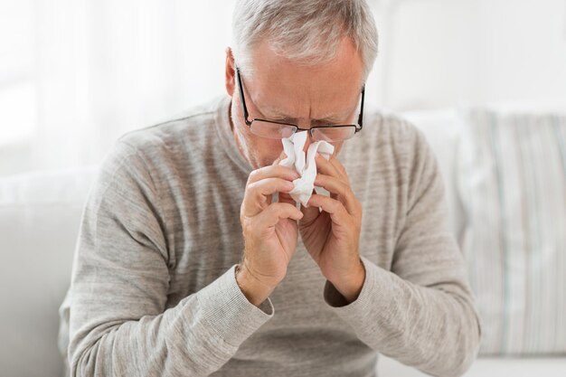 un homme âgé malade avec une serviette de papier qui se mouche le nez