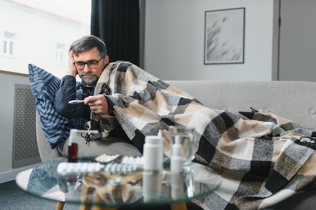 Homme âgé malade utilisant un thermomètre vérifiant sa température souffrant de grippe saisonnière ou de rhume