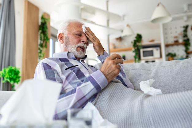 Homme âgé malade vérifiant sa température souffrant de grippe saisonnière ou de froid allongé sur un canapé souffrant de grippe saisonnière ou de rhume