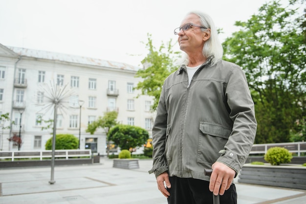 Un homme âgé marche avec une canne dans un parc de printemps de la ville