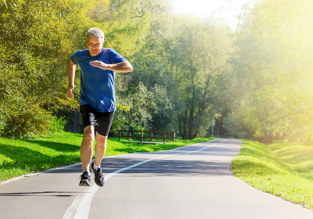 Homme d'âge moyen actif jogging dans un parc public pendant l'entraînement du matin