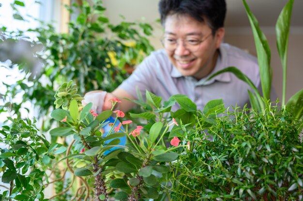 Un homme d'âge moyen asiatique qui sourit tout en prenant soin d'un parterre de fleurs à la maison.