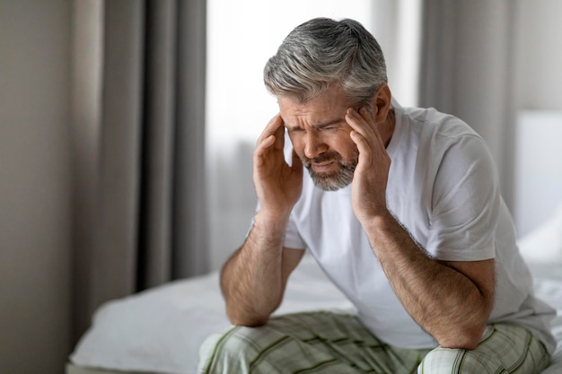 Homme d'âge moyen assis sur le lit touchant sa tête