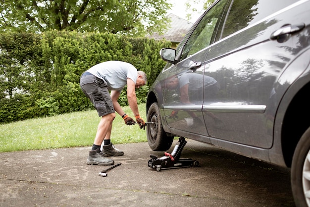 Un homme d'âge moyen aux cheveux gris change les pneus de la fourgonnette de sa famille.