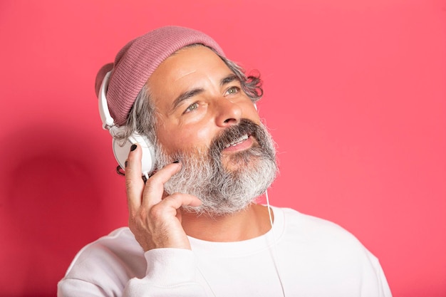 Homme d'âge moyen aux cheveux gris foncé 40s 50s en pull décontracté écoutant de la musique avec un casque isolé sur fond rose portrait en studio