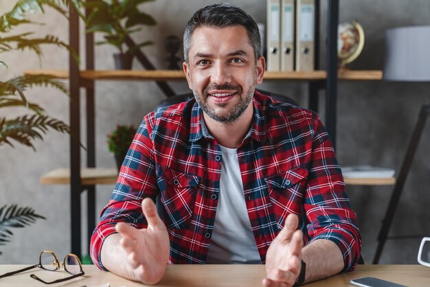 Homme d'âge moyen aux cheveux gris regarde la caméra parle avec son partenaire assis à table