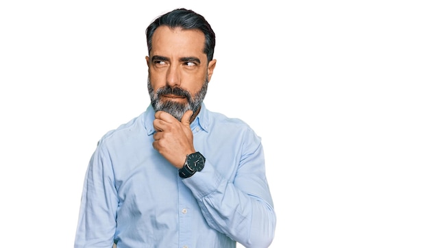 Homme d'âge moyen avec une barbe portant une chemise d'affaires pensant inquiet d'une question préoccupé et nerveux avec la main sur le menton