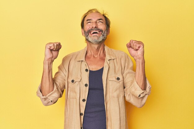 Photo homme d'âge moyen caucasien en studio jaune célébrant une passion et un enthousiasme de victoire