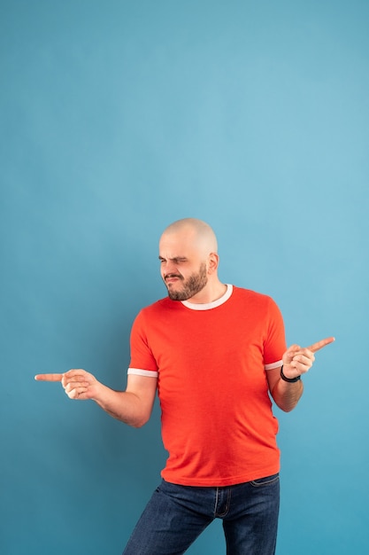 Un homme d'âge moyen chauve avec une barbe dans un t-shirt rouge sur fond bleu se tient les bras tendus et se réjouit de la victoire. Isolé.