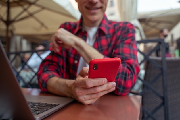 Homme d'âge moyen en chemise à carreaux assis à la table dans le café de la rue avec un téléphone dans les mains