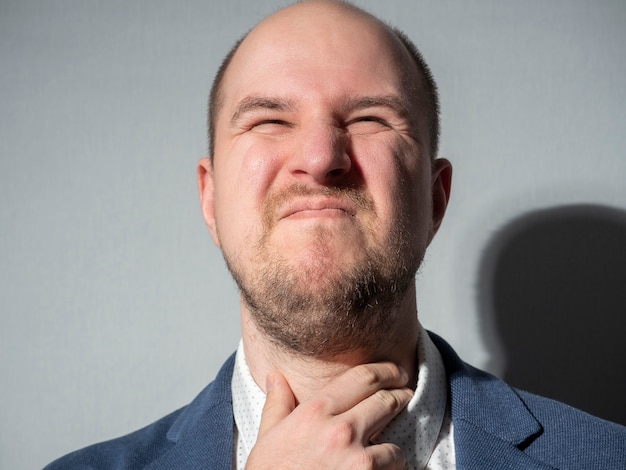 Un homme d'âge moyen en costume se tient la gorge. Homme d'affaires, barbe, chauve, maladie, froid.