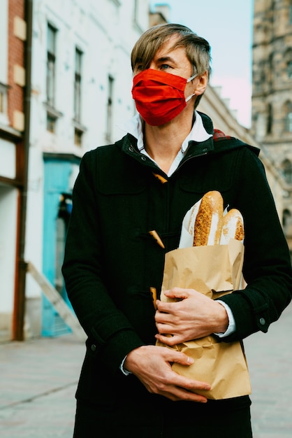 Photo homme d'âge moyen dans la rue avec du pain, de la baguette, des achats de pain pendant la pandémie mondiale, portant un masque, obtenant du pain de la boulangerie. plats à emporter, achats de boulangerie pendant covid 19.