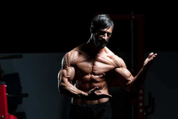 Homme d'âge moyen debout fort dans la salle de gym et muscles fléchissants - Modèle de forme physique de bodybuilder athlétique musclé posant après des exercices
