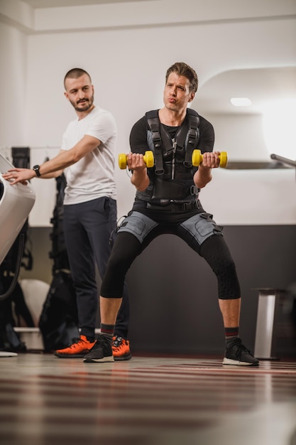 Un homme d'âge moyen fait de l'EMS avec un entraîneur personnel dans la salle de sport.