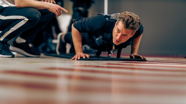 Un homme d'âge moyen fait des exercices de poussée pendant l'entraînement EMS dans la salle de sport.