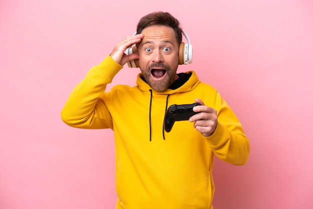 Homme d'âge moyen jouant avec un contrôleur de jeu vidéo isolé sur fond rose avec une expression surprise