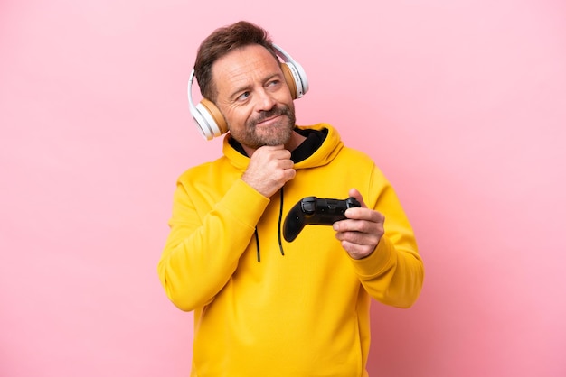 Homme d'âge moyen jouant avec un contrôleur de jeu vidéo isolé sur fond rose regardant en souriant