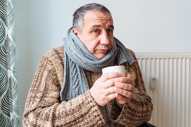 Un homme d'âge moyen malade vêtu de vêtements chauds se réchauffe avec du thé chaud