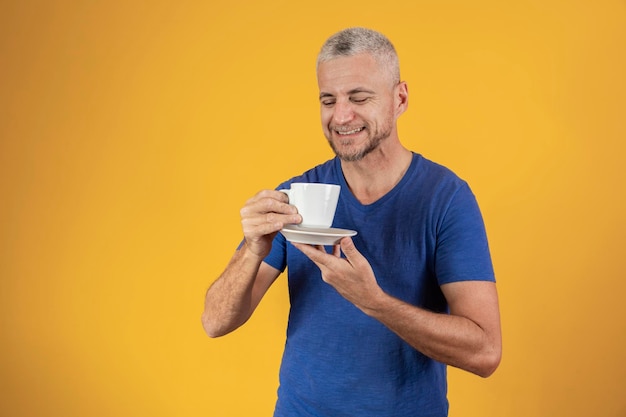 Homme d'âge moyen mature prenant un café ou un thé sur fond jaune avec espace libre pour le texte