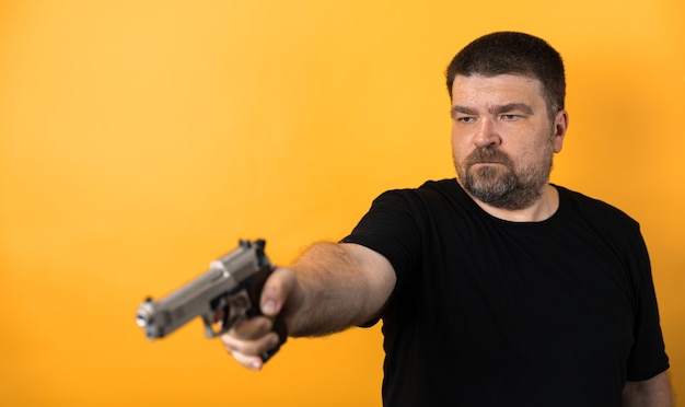 Photo homme d'âge moyen avec pistolet en t-shirt noir sur fond jaune.