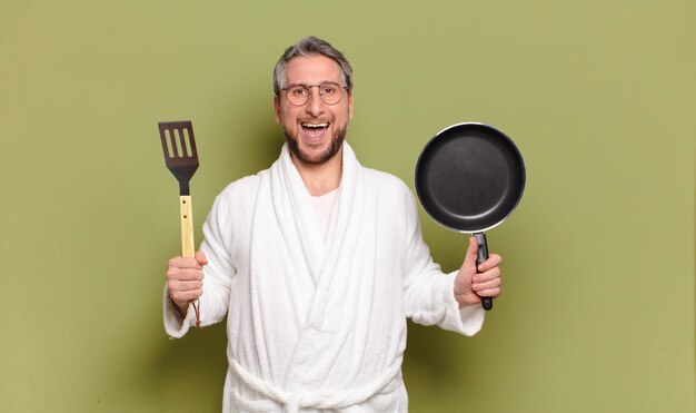 Homme d'âge moyen portant un peignoir et apprendre à cuisiner avec une casserole