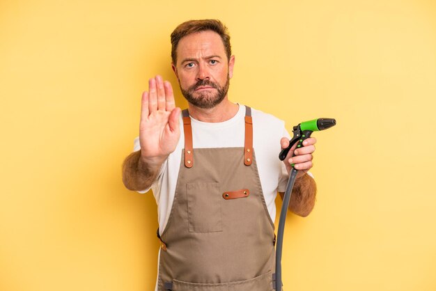 Homme d'âge moyen à la recherche de sérieux montrant la paume ouverte faisant un geste d'arrêt. concept de tuyau de jardinier