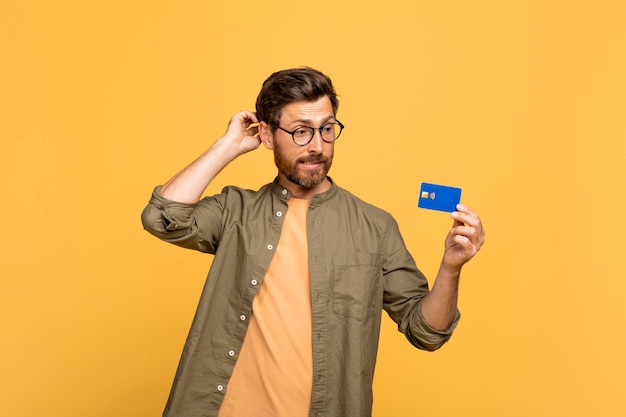 Un homme d'âge moyen réfléchi se gratte la tête, regarde sa carte de crédit et réfléchit à ses achats.