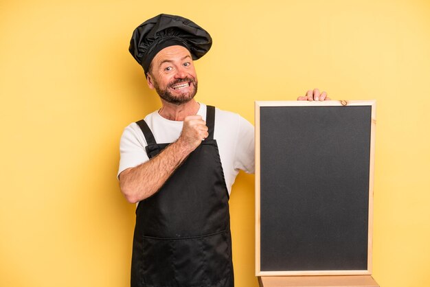 Homme d'âge moyen se sentant heureux et faisant face à un défi ou célébrant le concept de chef et de tableau noir