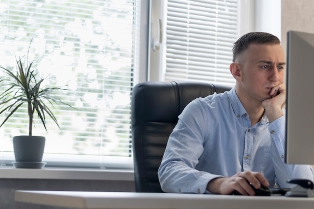 Un homme d'âge moyen sérieux travaille au bureau à l'ordinateur. Le directeur est dans son fauteuil. Le patron se concentre sur le projet.