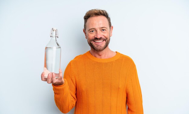 Homme d'âge moyen souriant joyeusement avec une main sur la hanche et confiant. concept de bouteille d'eau