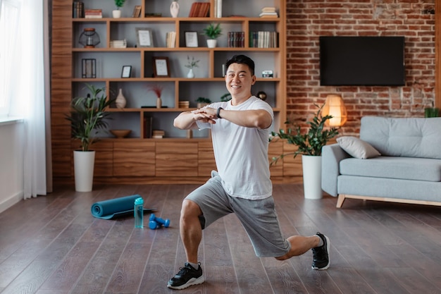 Homme d'âge mûr asiatique athlétique faisant des fentes faisant des exercices travaillant les muscles des jambes à la maison et souriant à la caméra