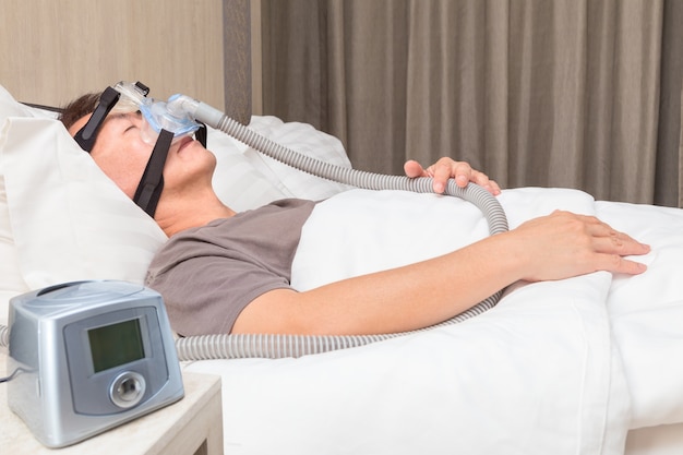 homme d&#39;âge mûr asiatique dormant dans son lit portant un masque CPAP se connectant à un tuyau d&#39;air et CPAP