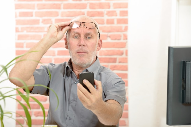 Photo homme d'âge mûr ayant des difficultés à voir l'écran du téléphone en raison de problèmes de vision