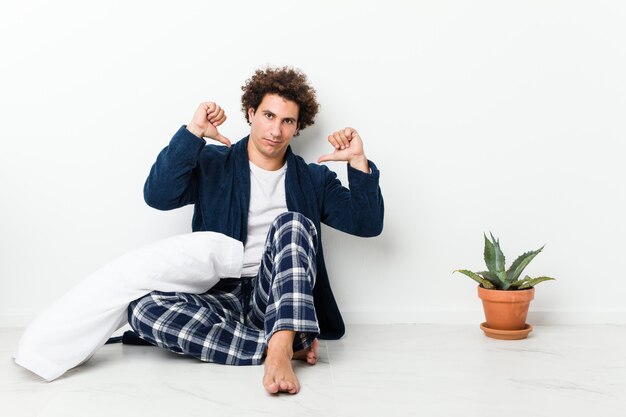 Un homme d'âge mûr portant un pyjama assis sur le sol de la maison se sent fier et confiant, exemple à suivre.