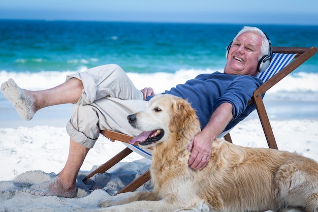 Homme d'âge mûr se reposant sur une chaise longue en écoutant de la musique caressant son chien